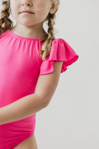 Child wearing a bright pink leotard with ruffled sleeves on a plain background