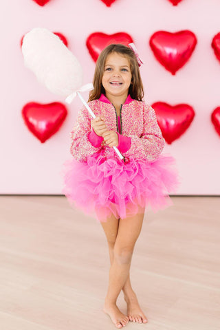 Young girl in a pink outfit with a tutu standing in front of a heart-themed backdrop.
