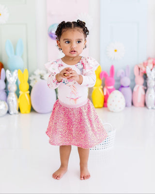 Child in a pink outfit standing in front of colorful Spring decorations.