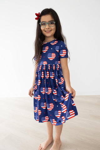 Young girl wearing a blue dress with American flag pattern on a white background