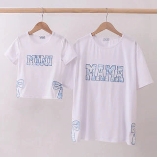 Two white t-shirts with 'MAMA' and 'MINI' text on a plain background