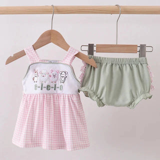 Baby’s outfit with pink checkered details and green bloomers on hangers against a light background
