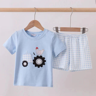 Children's blue t-shirt with tractor design and checkered shorts on a wooden hanger against a beige background.