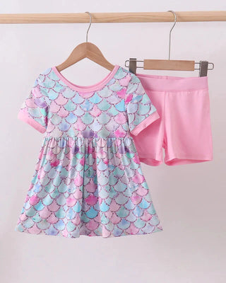 Children's outfit with a patterned dress and pink shorts on a hanger against a white background
