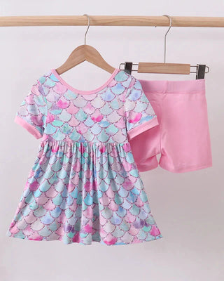 Children's outfit with a colorful dress and pink shorts on hangers against a white background