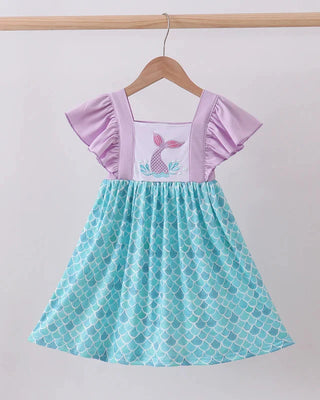Children's dress with mermaid design on a hanger against a plain background