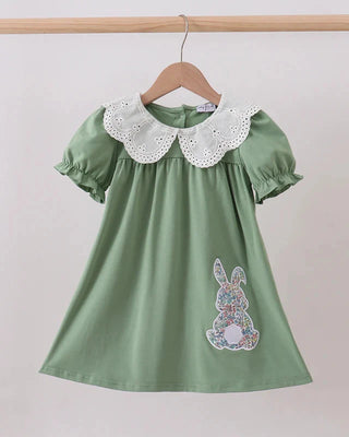 Green dress with floral bunny design and lace collar on a wooden hanger against a white background