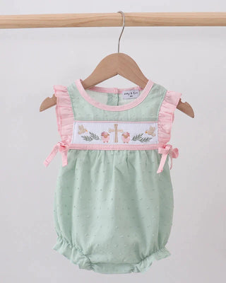 Green baby romper with pink ruffles and embroidered design on a wooden hanger against a white background.