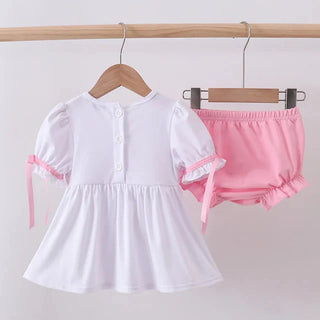 White dress with pink accents and pink shorts on hangers against a white background