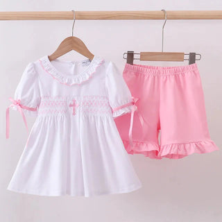 White top with lace details and pink shorts on hangers against a light gray background