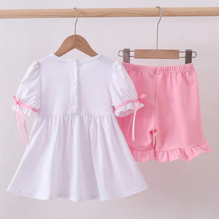 White top with pink accents and pink shorts on hangers against a white background
