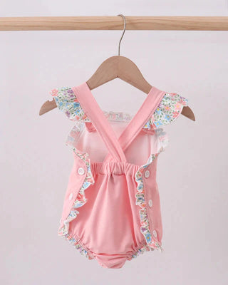 Pink baby romper with floral details on a wooden hanger against a light background