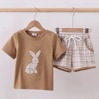 Children's brown t-shirt with bunny design and checkered shorts on hangers against a white background