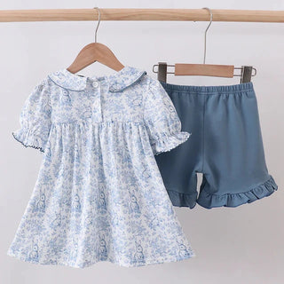 Children's floral dress and denim shorts on hangers against a white background