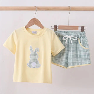 Children's yellow t-shirt with bunny design and green plaid shorts hanging on a rack.