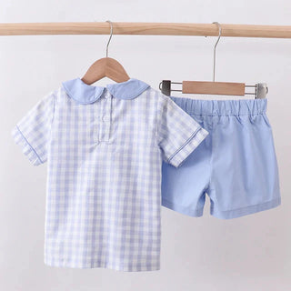 Children's blue checkered shirt and shorts set on hangers against a white background
