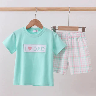 Children's mint green t-shirt with 'I ❤️ DAD' text and checkered shorts on a wooden hanger against a light gray background.
