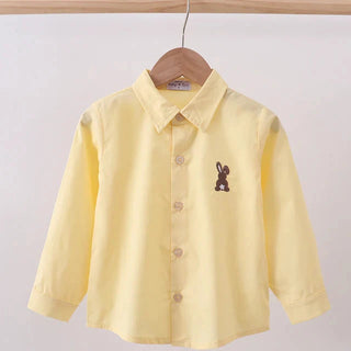 Yellow shirt with a small embroidered design on a hanger against a plain background