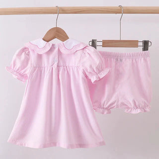 Pink baby dress and bloomers set on hangers against a light gray background
