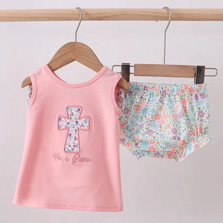 Pink tank top with floral cross design and matching shorts on hangers against a gray background