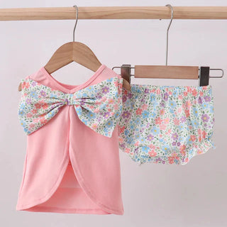 Pink top with floral bow and matching shorts on a hanger against a light gray background