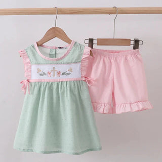 Children's green top with pink ruffled shorts on hangers against a light background