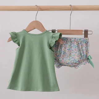 Green top and floral shorts set hanging on a wooden rack against a plain background