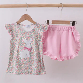 Children's floral top and pink shorts on hangers against a white background