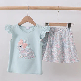 Children's outfit with light blue top and floral skirt on hangers against a white background