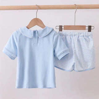 Children's light blue checkered shirt and shorts set on hangers against a plain background