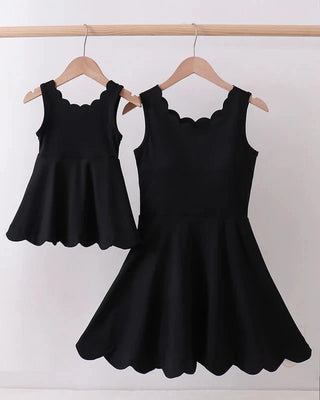 Black sleeveless dress with scalloped edges on hangers against a white background