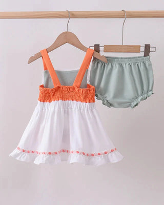 Children's outfit with orange top and white skirt hanging on a rack against a plain background