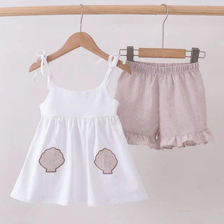 White top with shell designs and tan shorts on a wooden hanger against a white background