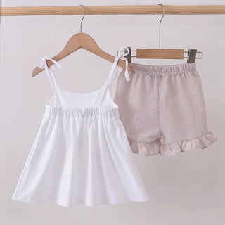White sleeveless top and tan shorts hanging on a wooden rack against a white background