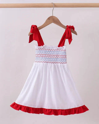 White dress with red accents hanging on a wooden hanger against a light background