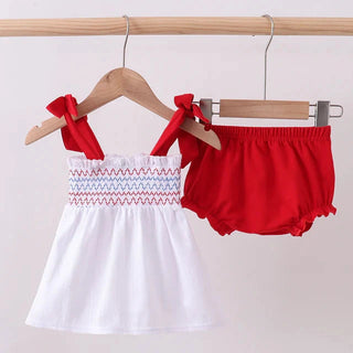 White top with red smocking and red bloomers on hangers against a white background