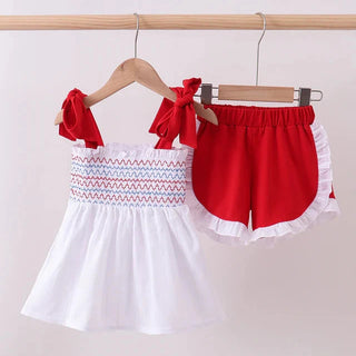 Children's outfit with white top and red shorts on hangers against a plain background