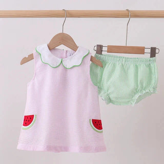Baby’s pink set with watermelon design and green checkered bloomers on hangers against a light background