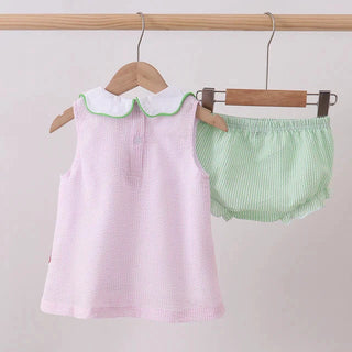 Pink baby set with green trim and matching bloomers on hangers against a light gray background