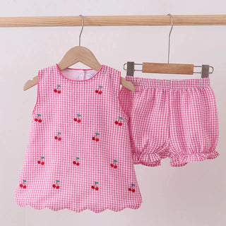 Pink checkered children's outfit with cherry pattern on a wooden hanger against a light pink background