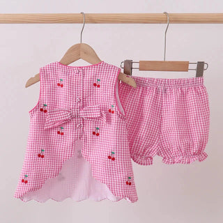 Pink gingham children's outfit with cherry details on a wooden hanger against a light background