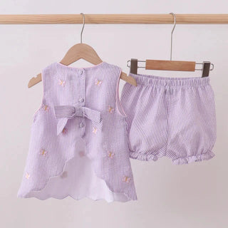 Baby’s outfit with a top and shorts on hangers against a plain background