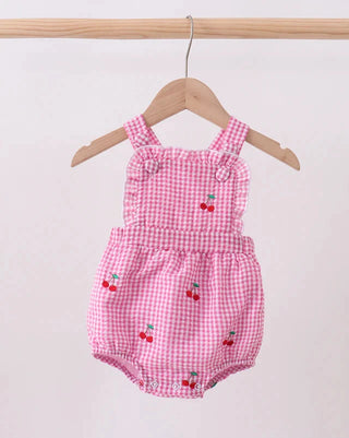 Pink checkered baby romper with cherry designs on a wooden hanger against a white background