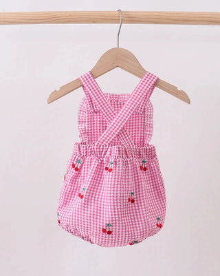 Pink gingham baby romper with cherry pattern on a wooden hanger against a white background