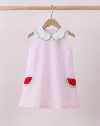 Pink dress with watermelon designs on a hanger against a plain background
