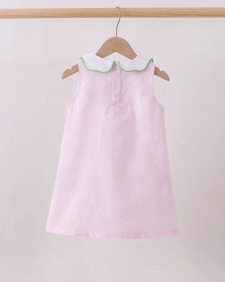 Pink dress with a white collar on a wooden hanger against a light gray background