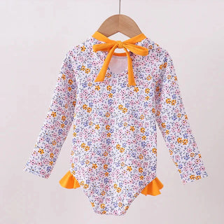 Floral swimsuit with orange accents on a wooden hanger against a light background