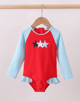 Red and light blue swimsuit with star design on a wooden hanger against a beige background