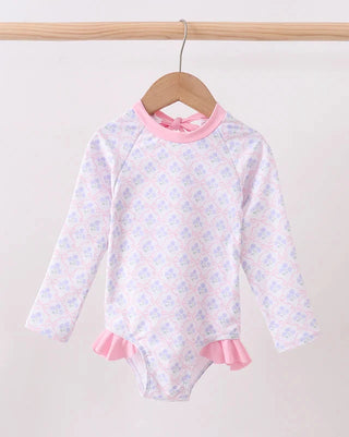 Swimsuit with floral pattern and pink trim on a wooden hanger against a white background