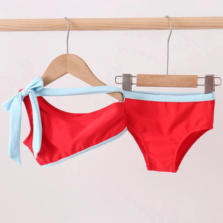 Red bikini with blue straps hanging on a wooden rack against a light background